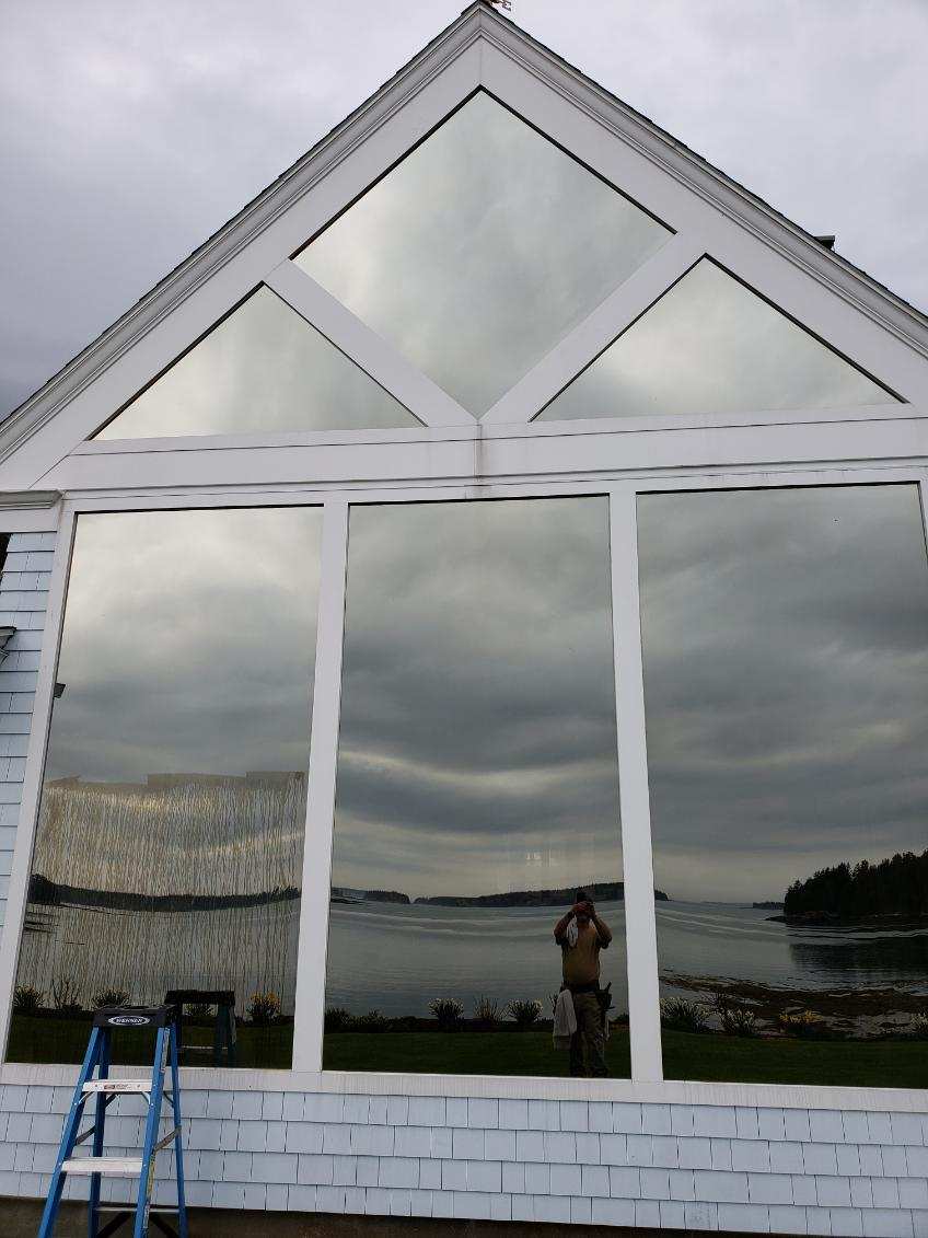 Sun Services technician cleaning a large gable-end window on a coastal Maine home